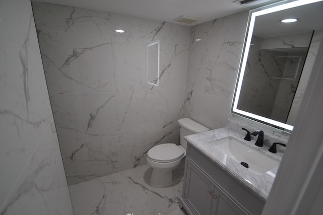 bathroom featuring visible vents, toilet, stone wall, and vanity