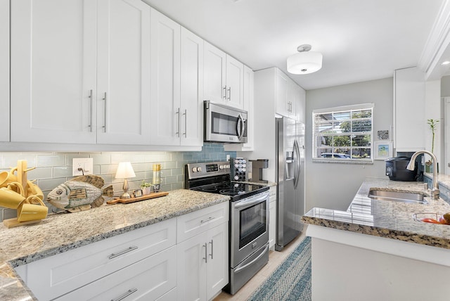 kitchen with light stone counters, decorative backsplash, white cabinets, stainless steel appliances, and a sink