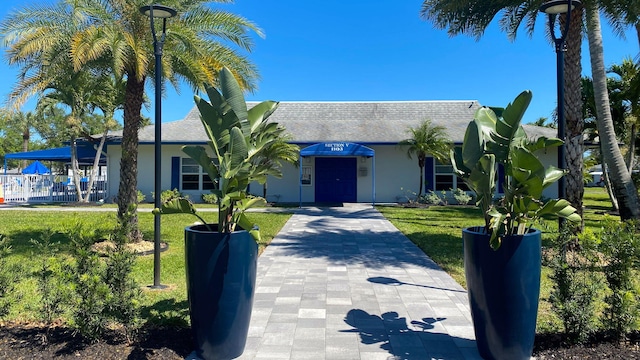 view of front of property with stucco siding, a shingled roof, and a front yard