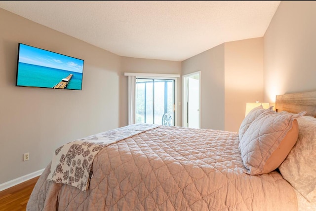 bedroom with wood finished floors, baseboards, and a textured ceiling