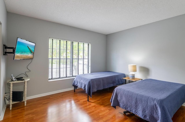 bedroom featuring baseboards, a textured ceiling, and wood finished floors