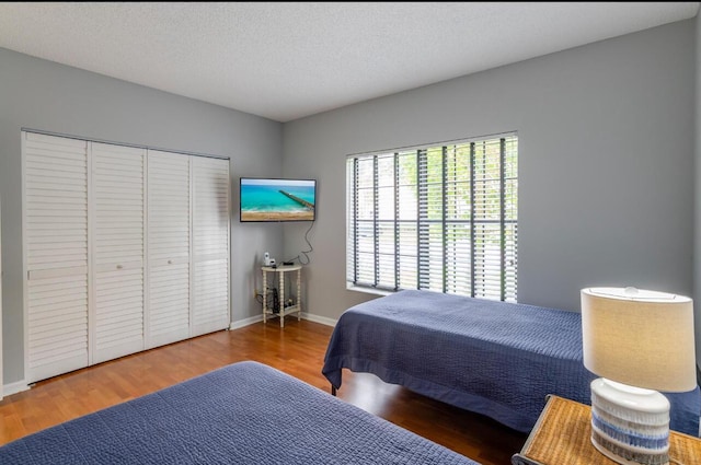 bedroom featuring a closet, baseboards, a textured ceiling, and wood finished floors