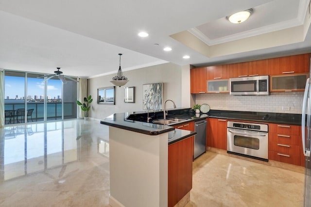 kitchen with a tray ceiling, brown cabinets, appliances with stainless steel finishes, and a sink