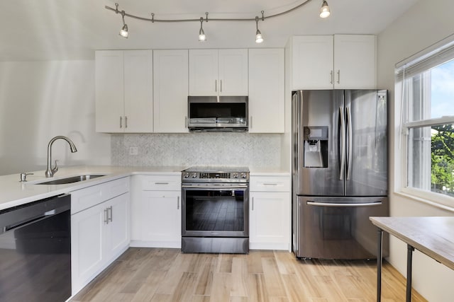 kitchen with light wood-type flooring, a sink, backsplash, white cabinetry, and appliances with stainless steel finishes