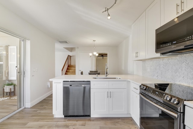 kitchen with visible vents, a peninsula, a sink, appliances with stainless steel finishes, and a chandelier