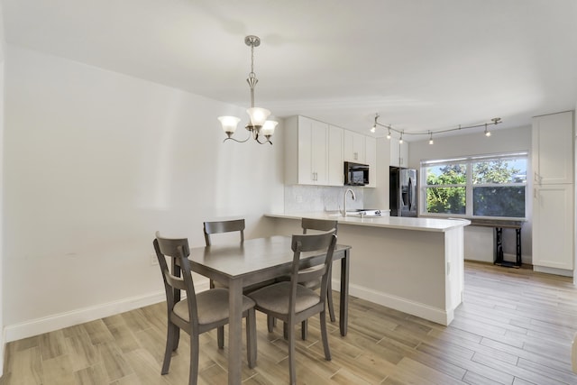 dining area featuring track lighting, baseboards, light wood-type flooring, and an inviting chandelier