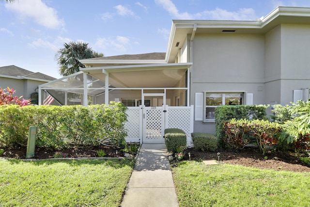 view of front of property featuring stucco siding, glass enclosure, a front yard, and roof with shingles