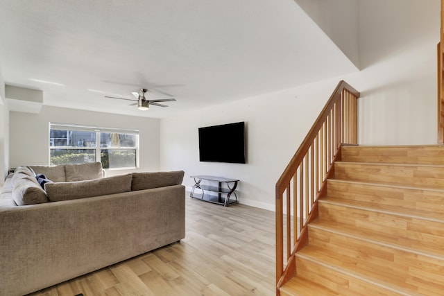 living room featuring stairway, light wood-style flooring, baseboards, and a ceiling fan