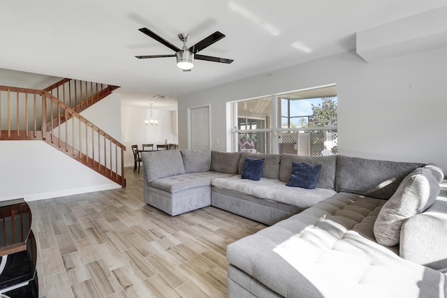 living room with stairs, ceiling fan with notable chandelier, baseboards, and light wood finished floors