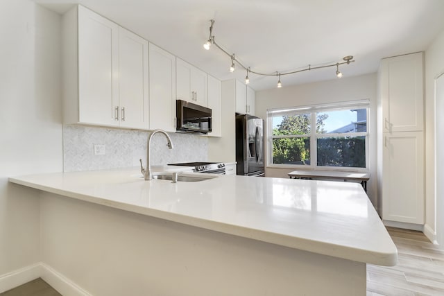 kitchen with tasteful backsplash, black microwave, a peninsula, stainless steel fridge, and a sink