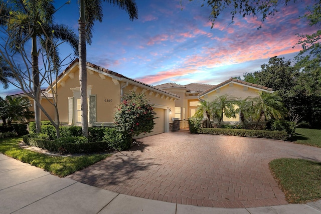 mediterranean / spanish-style house with decorative driveway, a tile roof, an attached garage, and stucco siding