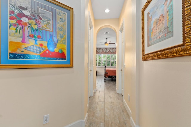 corridor featuring light wood-type flooring, baseboards, arched walkways, and visible vents