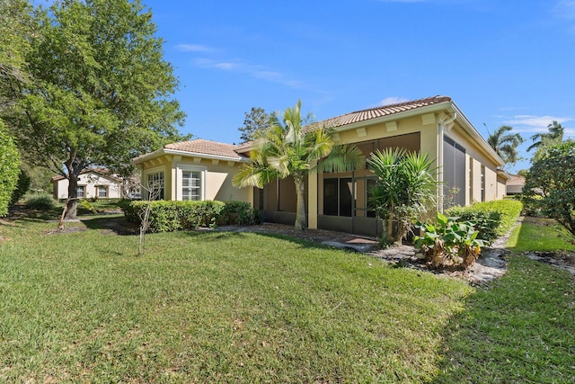 back of house with stucco siding, a tiled roof, a lawn, and a sunroom