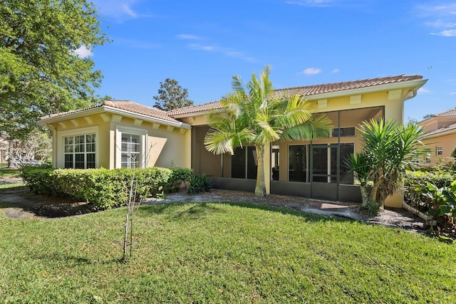 back of house with a yard, a sunroom, stucco siding, and a tiled roof