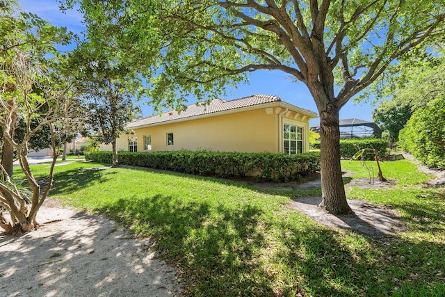 view of property exterior featuring stucco siding, a lawn, a lanai, and a tiled roof