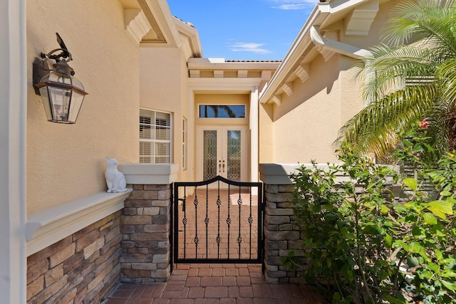 view of exterior entry featuring a gate, french doors, stone siding, and stucco siding