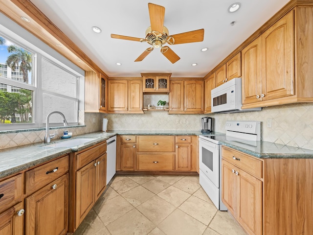 kitchen featuring glass insert cabinets, dark stone counters, decorative backsplash, white appliances, and a sink