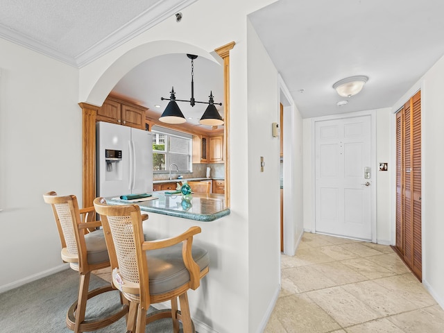 kitchen with backsplash, baseboards, a kitchen breakfast bar, white refrigerator with ice dispenser, and brown cabinetry