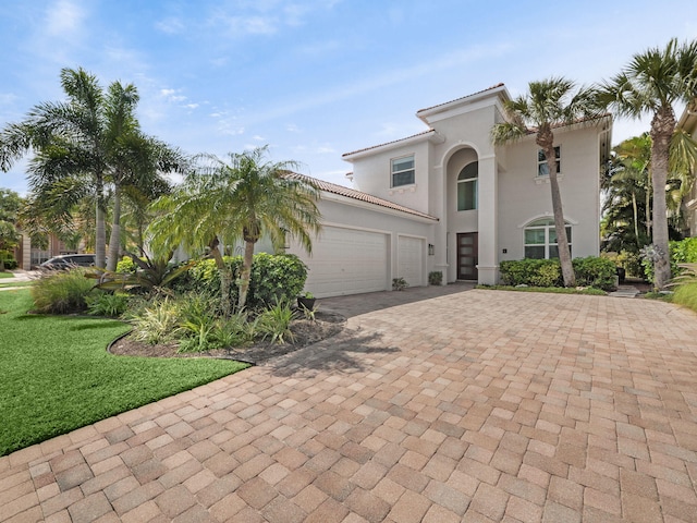 mediterranean / spanish-style home featuring a front lawn, a tile roof, stucco siding, decorative driveway, and a garage