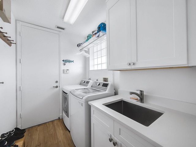 laundry area with wood finished floors, visible vents, cabinet space, a sink, and washing machine and dryer