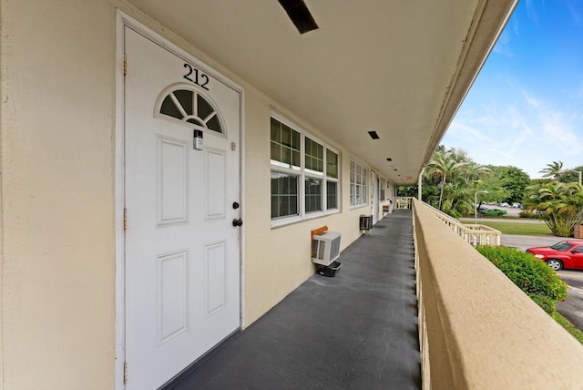 property entrance with stucco siding, an AC wall unit, and a balcony