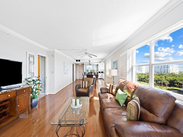 living area featuring light wood-type flooring, a textured ceiling, a ceiling fan, and crown molding