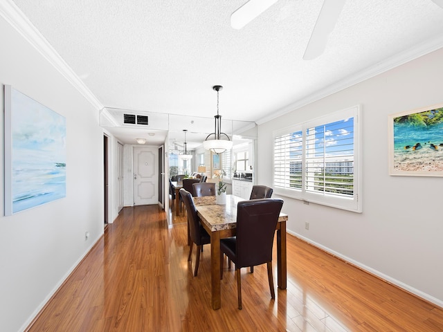 dining area featuring visible vents, a textured ceiling, wood finished floors, and ornamental molding