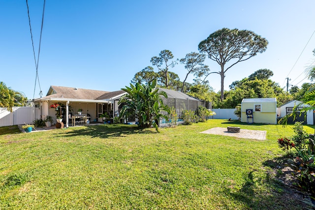 view of yard featuring a lanai, an outdoor fire pit, a fenced backyard, an outdoor structure, and a patio