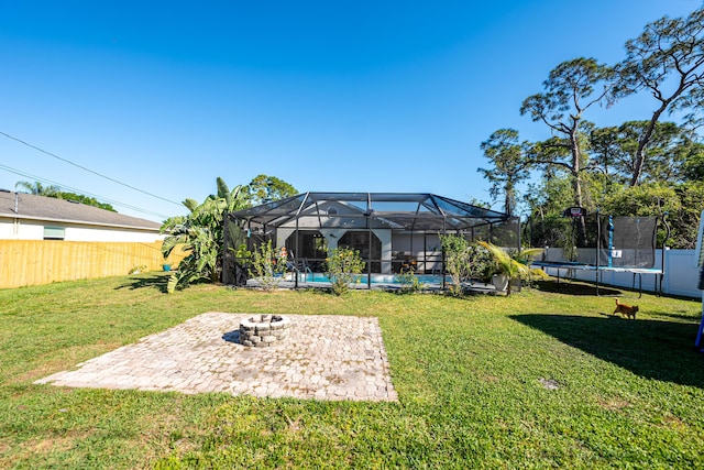 view of yard with glass enclosure, an outdoor fire pit, a fenced backyard, a trampoline, and a patio area