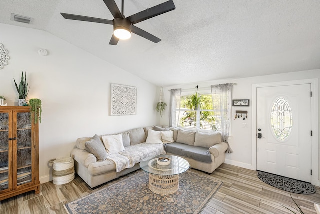 living area with visible vents, ceiling fan, vaulted ceiling, light wood-style floors, and a textured ceiling