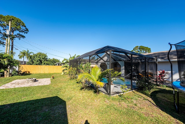 view of yard featuring a patio, a trampoline, fence, an outdoor fire pit, and glass enclosure