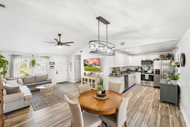 dining area with wood finish floors, visible vents, a textured ceiling, and vaulted ceiling