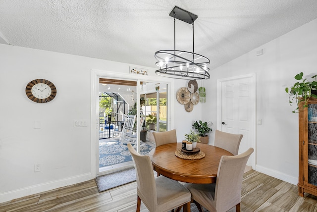 dining space featuring a chandelier, a textured ceiling, light wood-style flooring, and vaulted ceiling