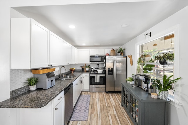 kitchen with dark stone counters, a sink, decorative backsplash, stainless steel appliances, and white cabinetry