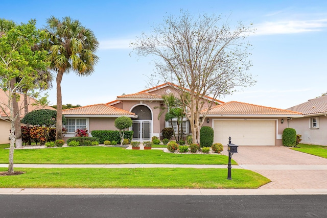 mediterranean / spanish home featuring a tiled roof, a front yard, stucco siding, decorative driveway, and a garage