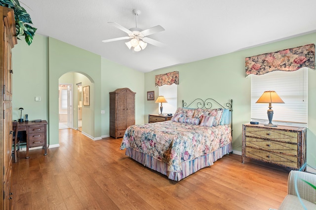 bedroom featuring wood finished floors, baseboards, lofted ceiling, arched walkways, and connected bathroom