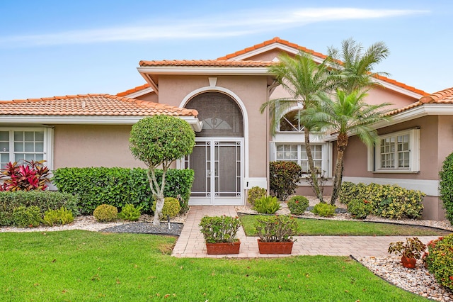 view of exterior entry with stucco siding, a tile roof, and a yard