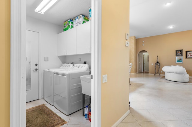 laundry area featuring baseboards, cabinet space, light tile patterned flooring, arched walkways, and independent washer and dryer