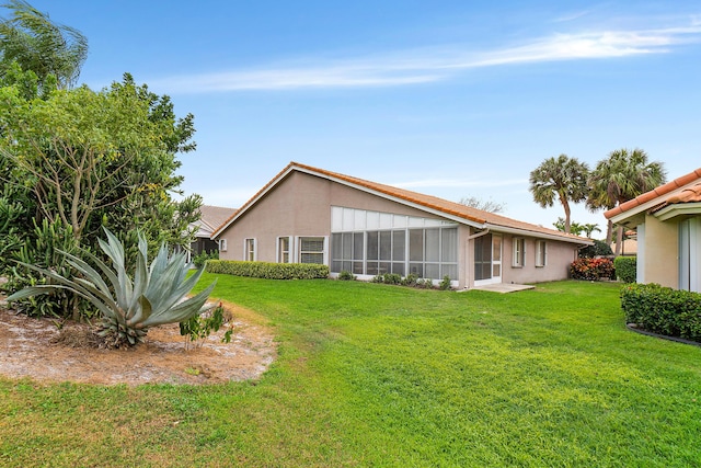 rear view of property featuring stucco siding, a lawn, and a sunroom