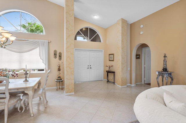 entrance foyer with baseboards, high vaulted ceiling, an inviting chandelier, light tile patterned flooring, and arched walkways