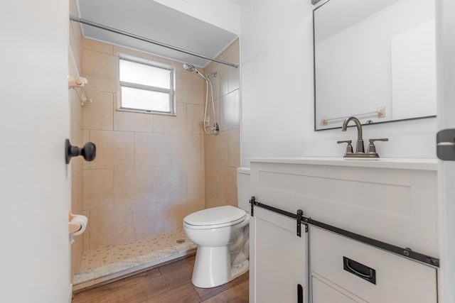 bathroom with vanity, toilet, wood finished floors, and a tile shower