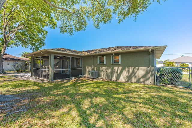 rear view of house with stucco siding, a lawn, fence, a sunroom, and central AC unit