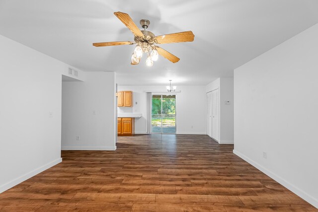 empty room featuring dark wood-style floors, visible vents, ceiling fan with notable chandelier, and baseboards