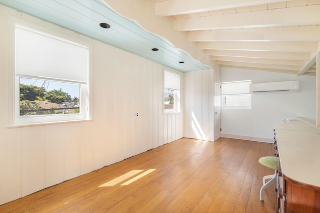 interior space featuring a wall mounted air conditioner, lofted ceiling with beams, light wood-style flooring, and a healthy amount of sunlight