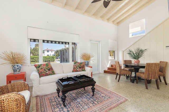 living area featuring beam ceiling, high vaulted ceiling, light speckled floor, ceiling fan, and stairs