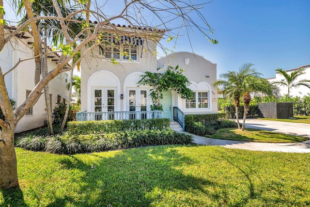 mediterranean / spanish-style home with a front lawn, fence, stucco siding, french doors, and driveway