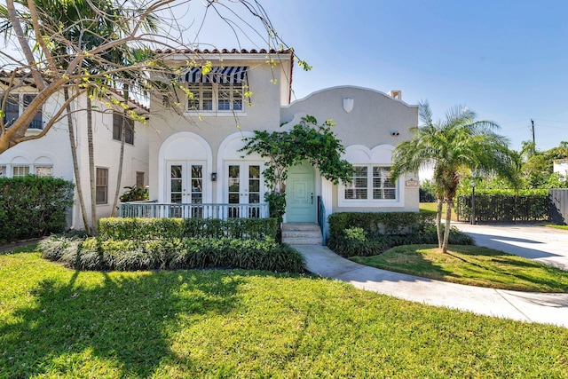 mediterranean / spanish home with a front lawn, fence, concrete driveway, stucco siding, and french doors