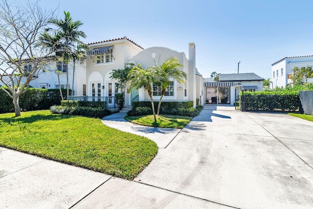 mediterranean / spanish house featuring a tiled roof, stucco siding, driveway, and a front yard