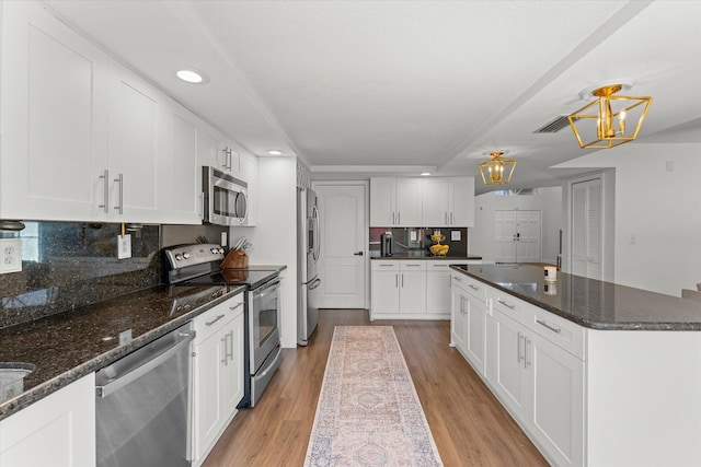 kitchen with light wood finished floors, a kitchen island, decorative backsplash, appliances with stainless steel finishes, and white cabinets