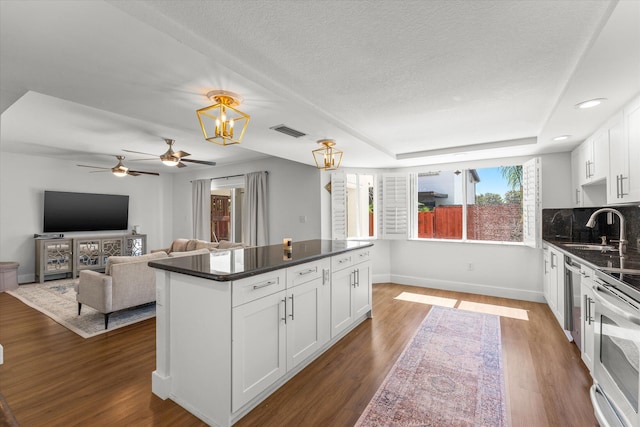 kitchen with wood finished floors, visible vents, a sink, decorative backsplash, and dark countertops